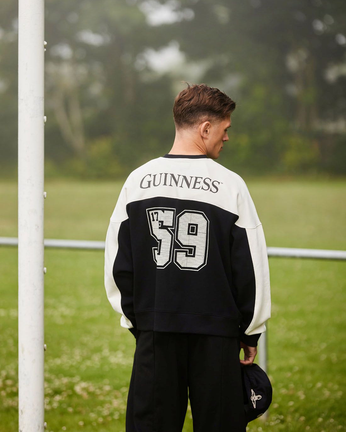 Person wearing a black and white jacket with 'Guinness' and number '59' on a grassy field.