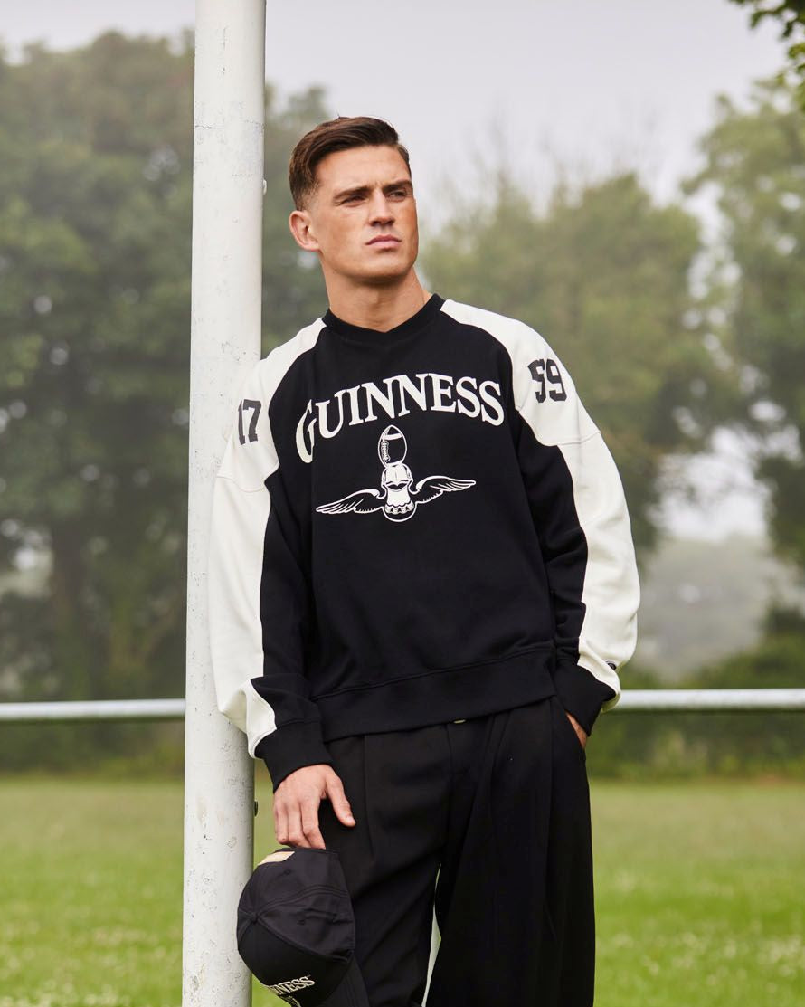 Man wearing a black and white Guinness sweatshirt on a grassy field.