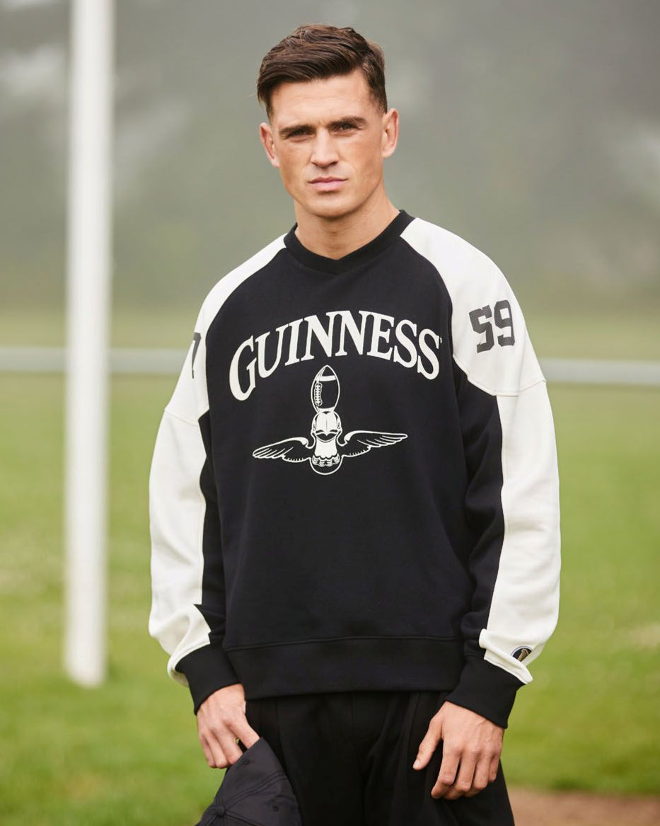Person wearing a black and white Guinness sweatshirt on a grassy field with a goalpost in the background.
