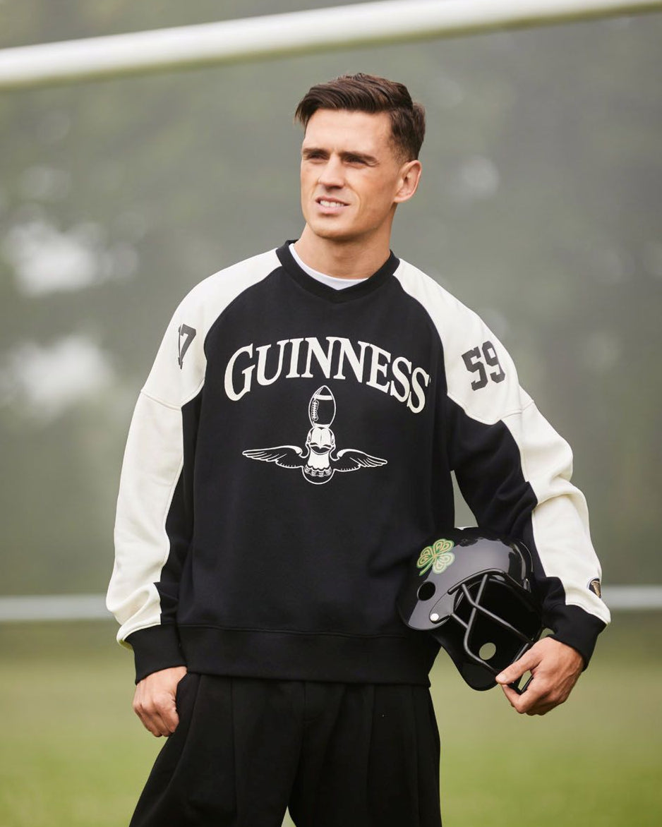 Man wearing a black and white Guinness sweatshirt with a helmet, standing on a soccer field.