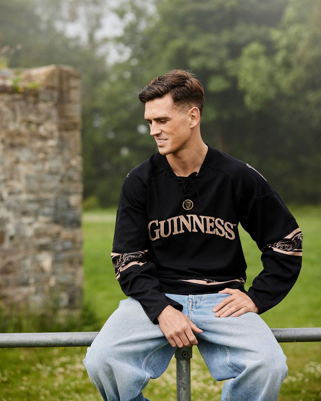 Man wearing a Guinness sweatshirt sitting outdoors with greenery in the background