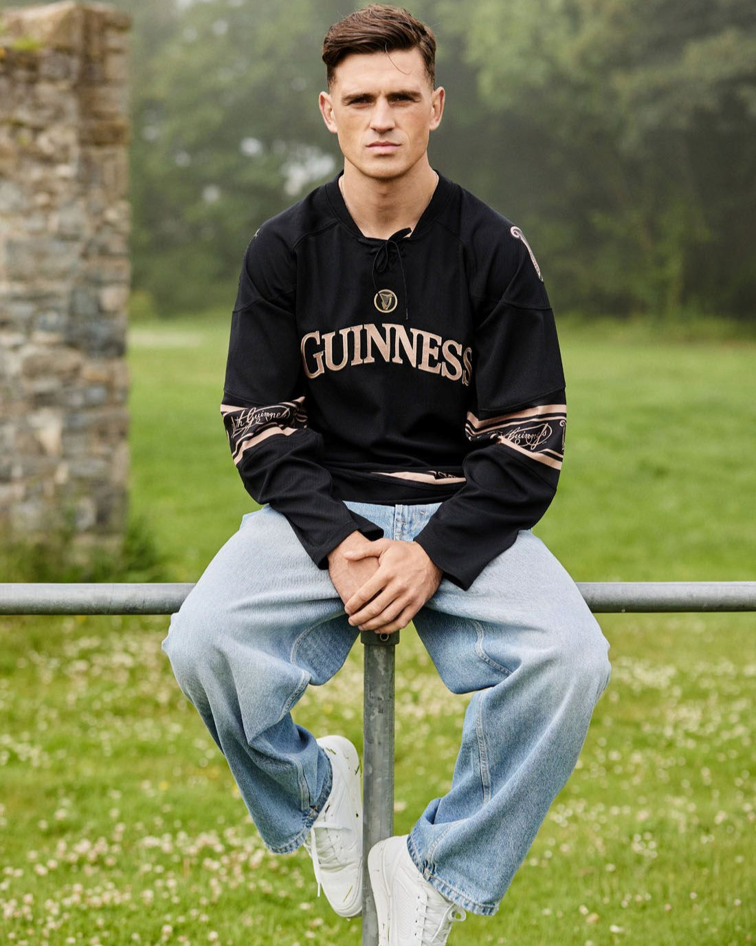 Person wearing a Guinness sweatshirt sitting on a metal railing in a park.