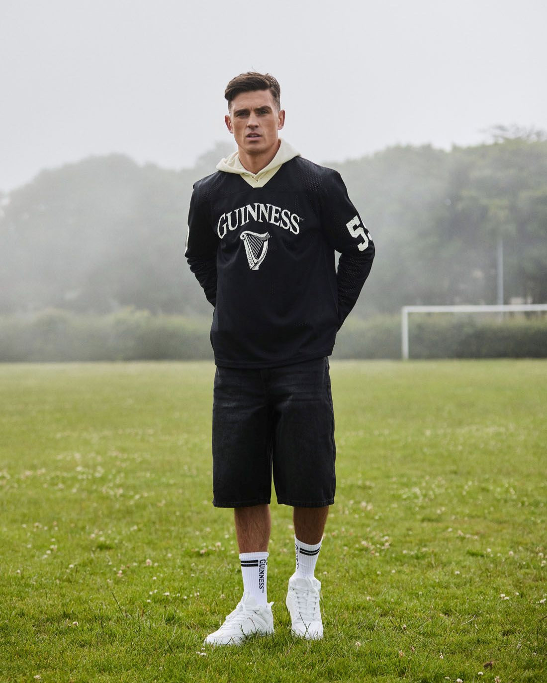 Person wearing a black Guinness hoodie and shorts on a grassy field