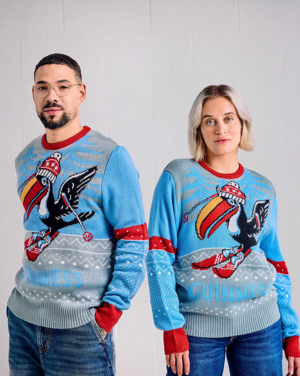 Two people wearing matching festive sweaters with a colorful design on a plain background
