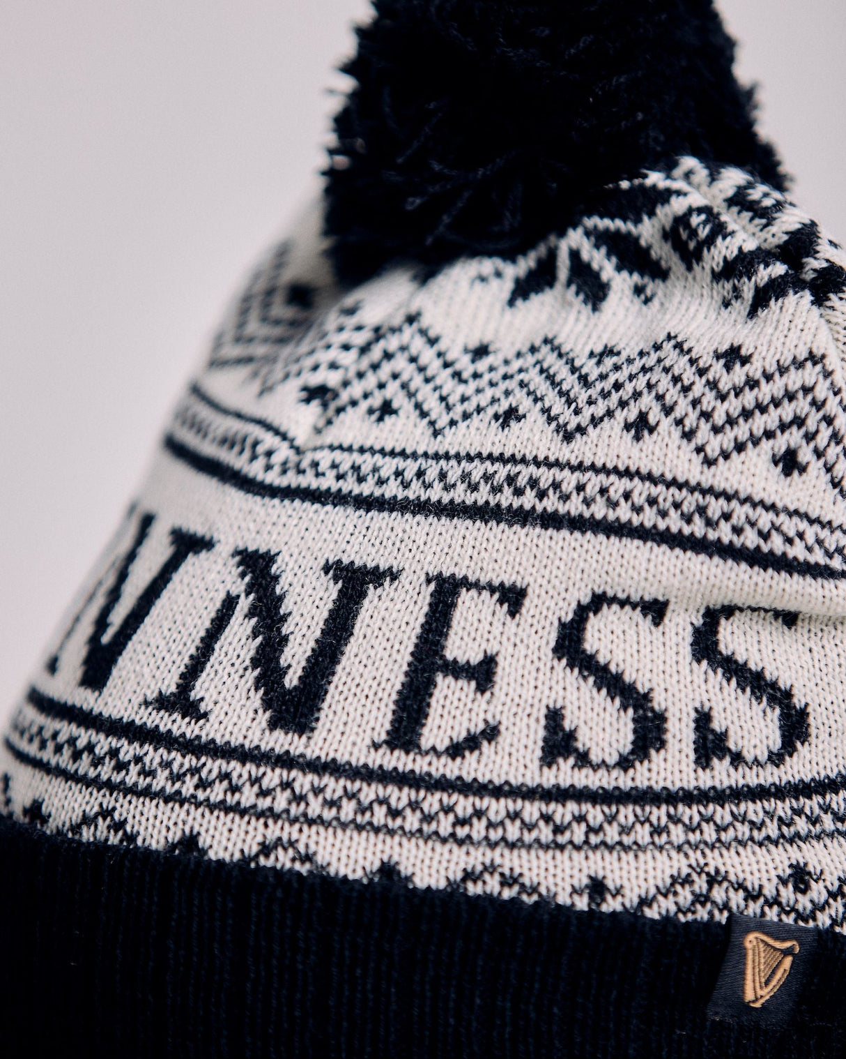 Knitted beanie with pom-pom and 'UNINESS' text on a light background