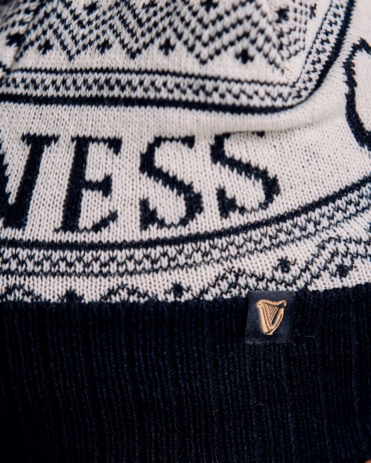 Close-up of a person wearing a black and white patterned beanie with 'Guess' branding.