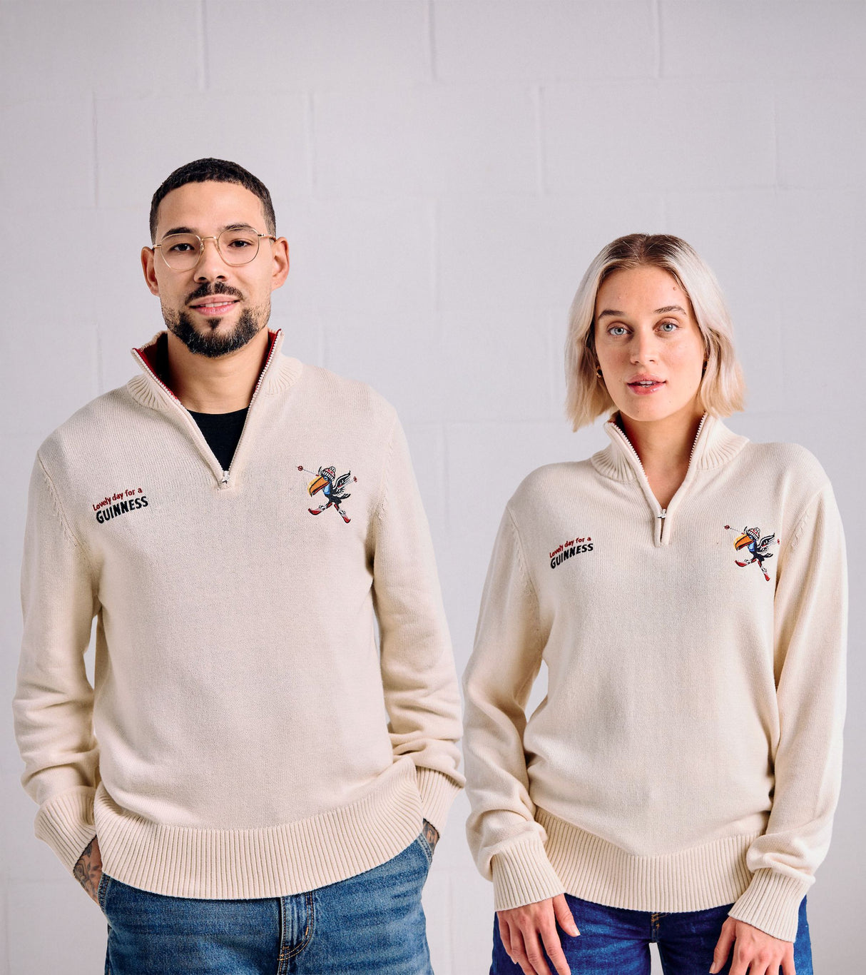 Two people wearing cream-colored sweaters with Guinness logo against a plain background