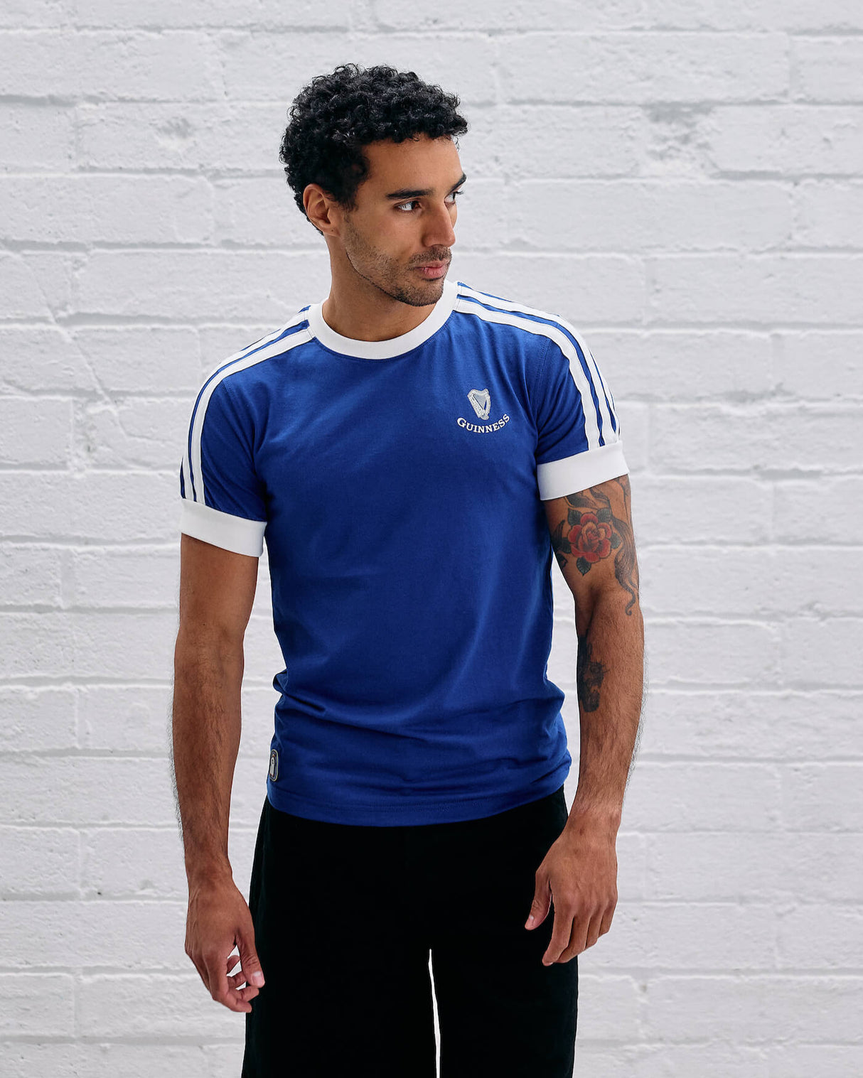 Man wearing a Guinness blue t-shirt with white stripes against a light gray brick wall