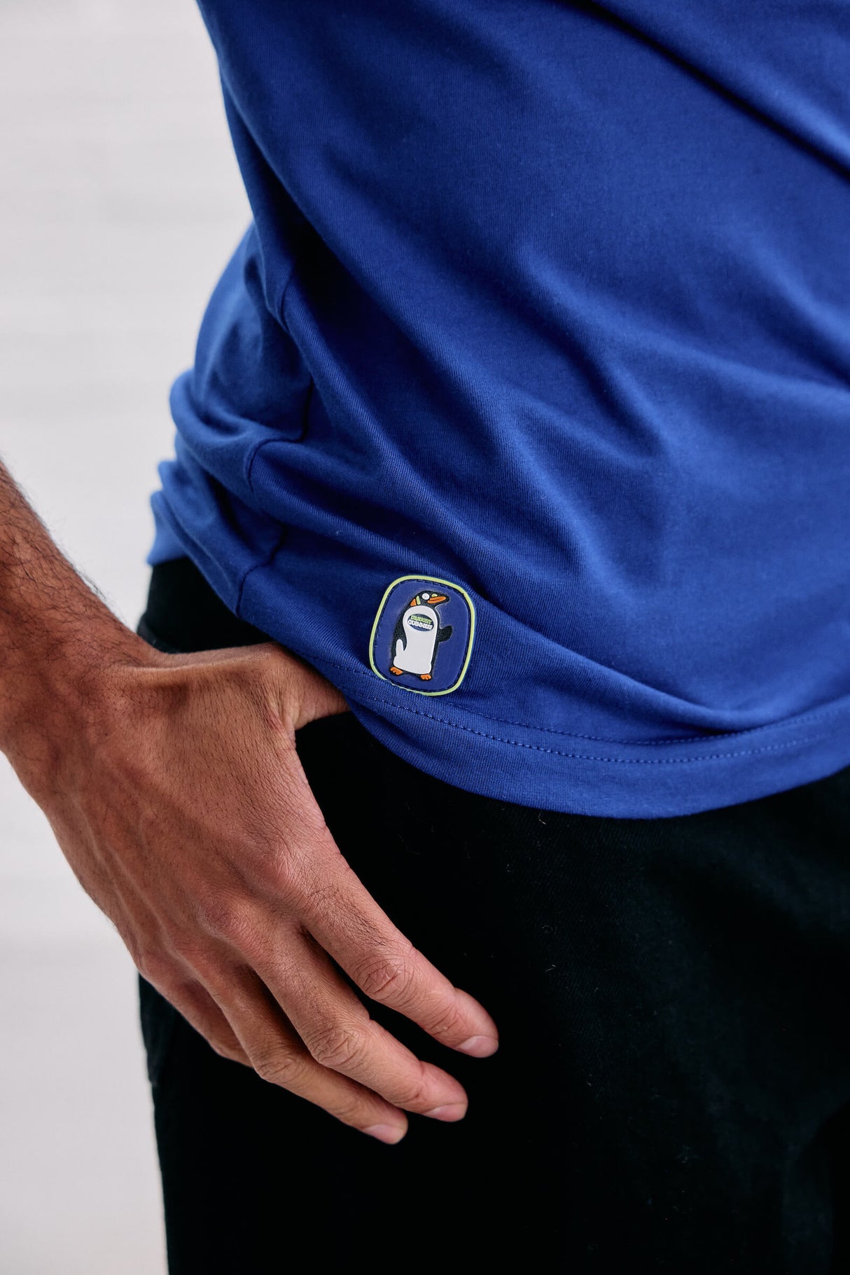 Blue shirt with a logo on a person wearing black pants against a light background