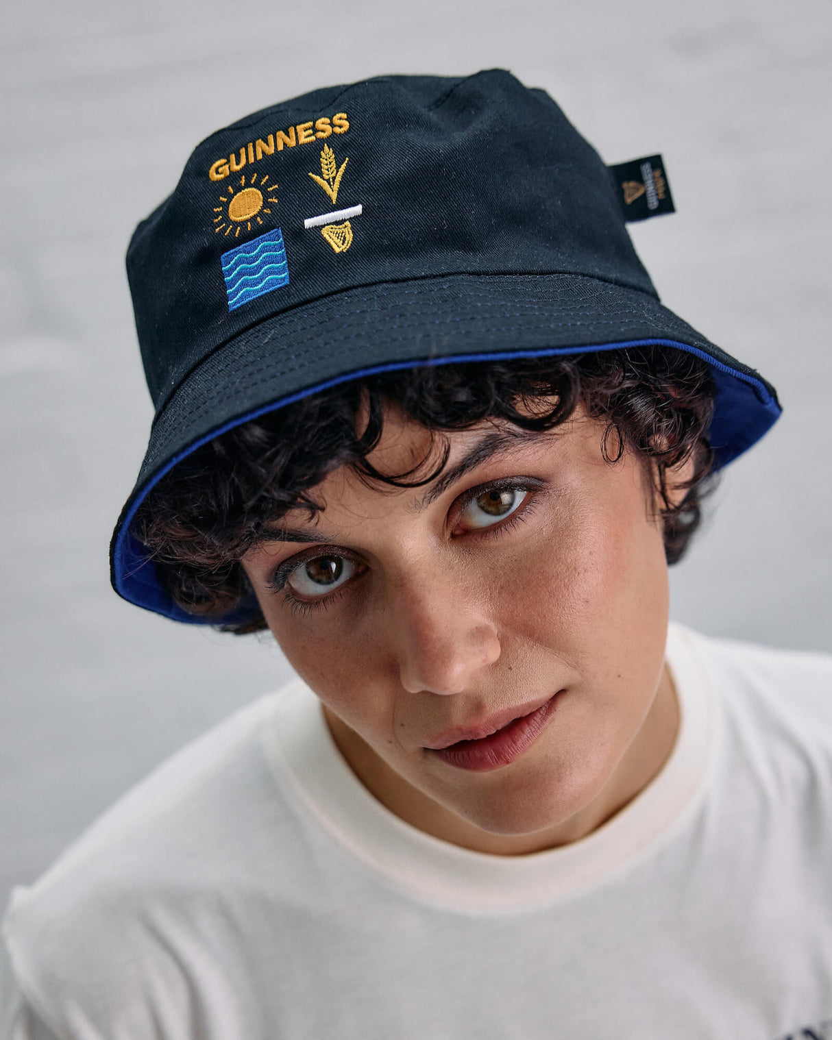 Person wearing a navy bucket hat with Guinness logo and symbols on a gray background