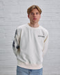 Man wearing a white Guiness sweatshirt against a white brick wall