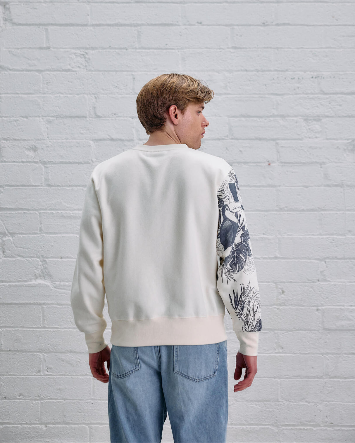 Person wearing a white sweater with floral sleeves against a light gray brick wall.