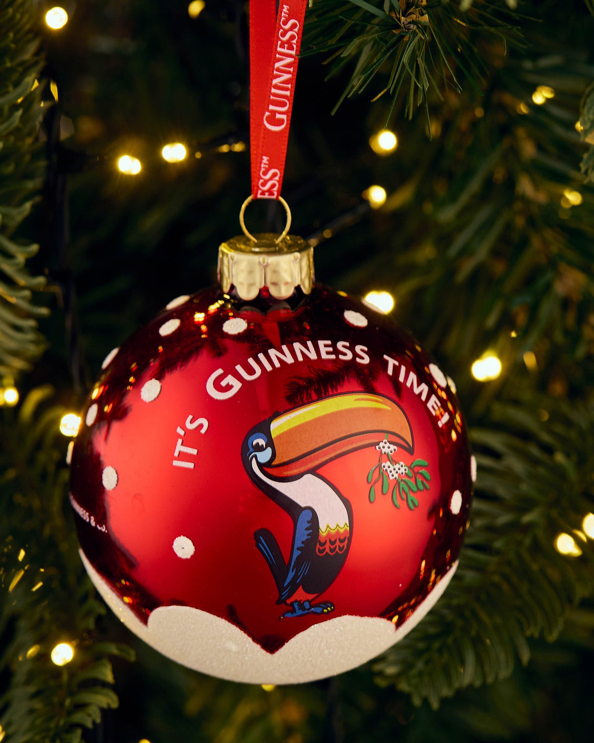 Red ornament with 'It's Guinness Time' text and toucan design on a Christmas tree.