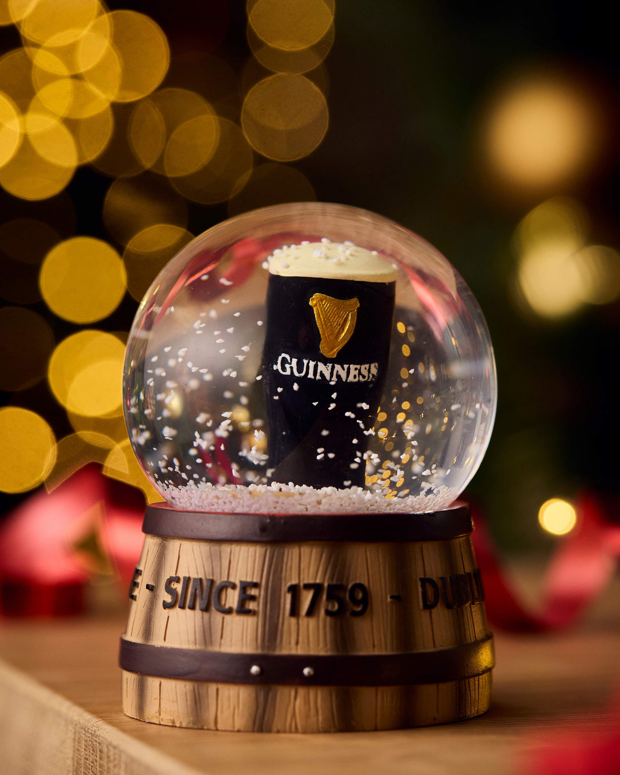 Snow globe with a Guinness pint shape inside, featuring the brand's logo and text, against a festive background.