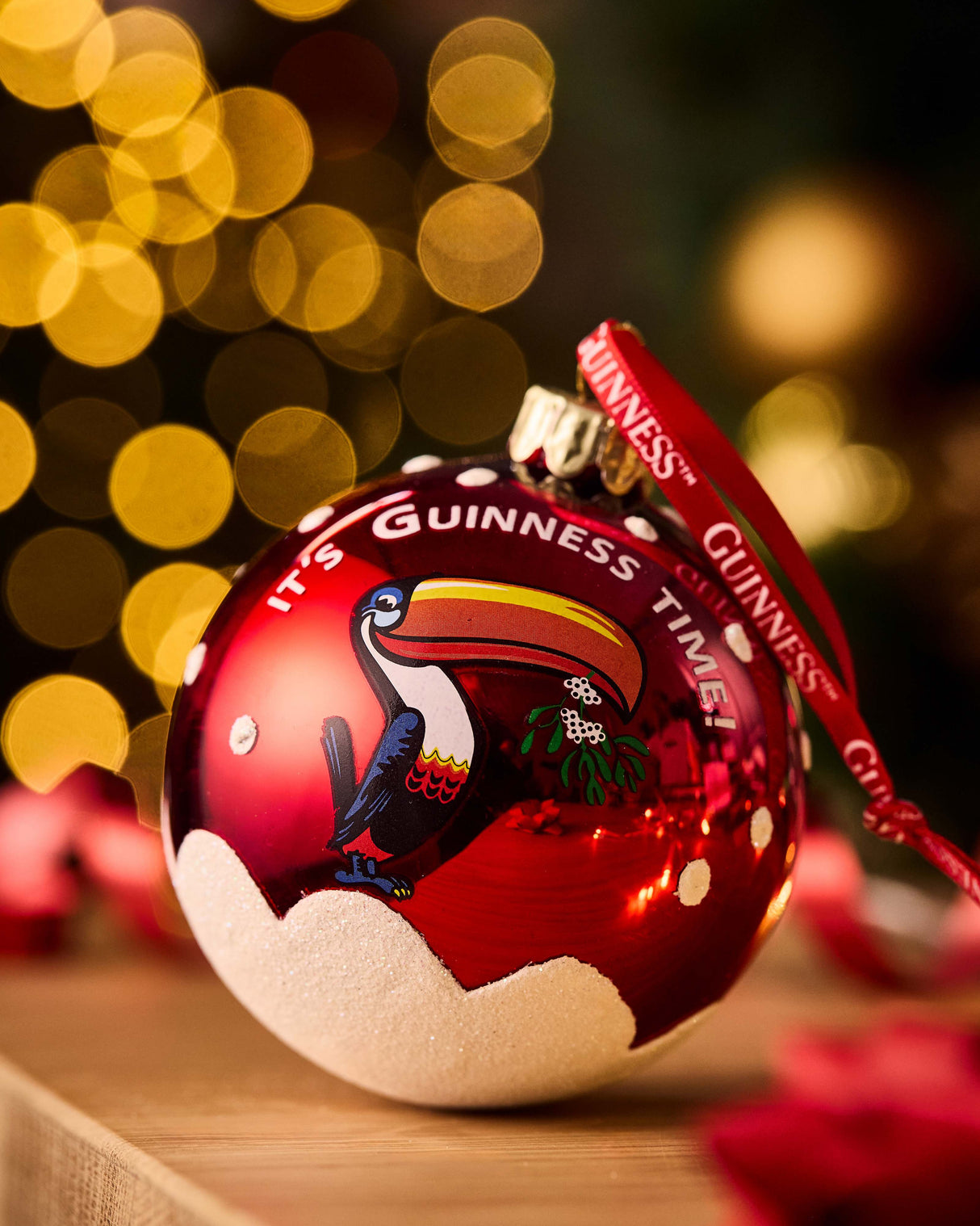 Red Christmas ornament with toucan design and 'Guinness' branding against a blurred festive background.