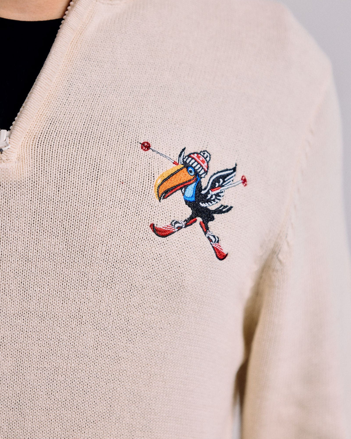 Beige sweater with a colorful embroidered design on a plain background