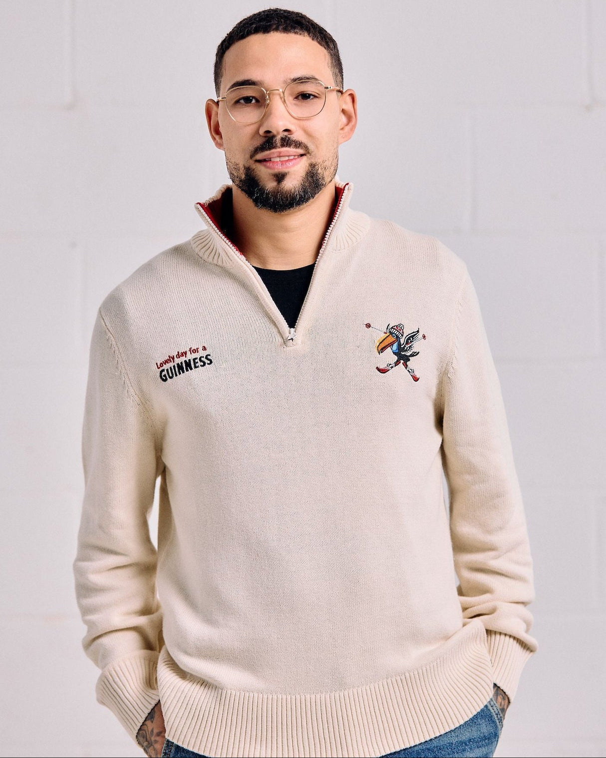 Man wearing a beige sweater with embroidered designs on a white background