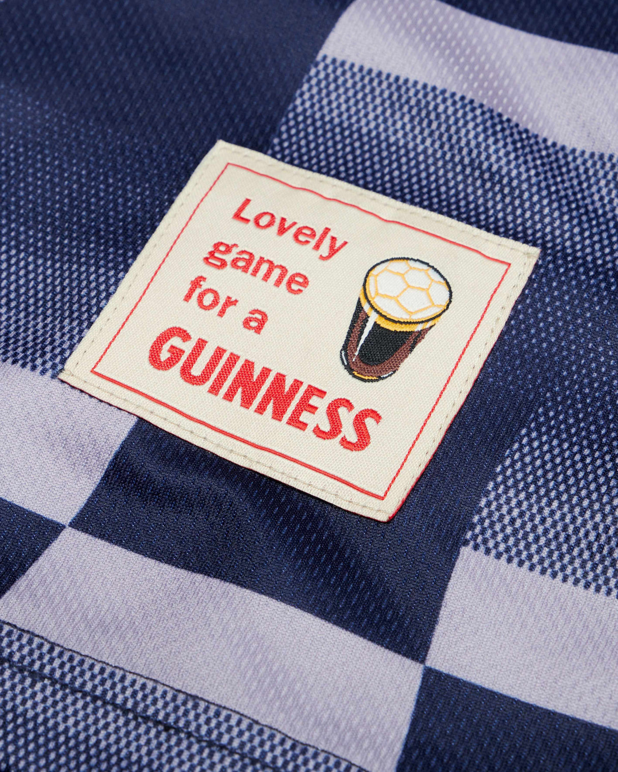 Label with 'Lovely game for a GUINNESS' text and beer graphic on a blue and white checkered fabric background
