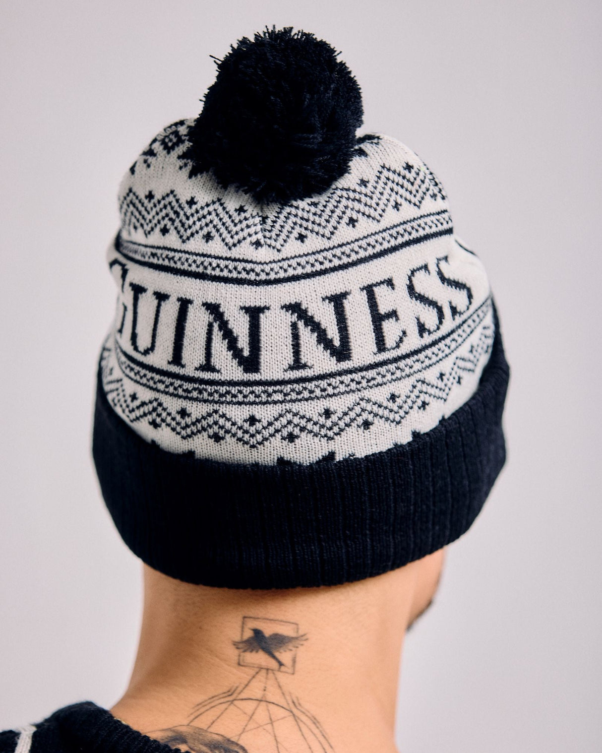 Person wearing a black and white knit beanie with 'Guinness' branding on a plain background