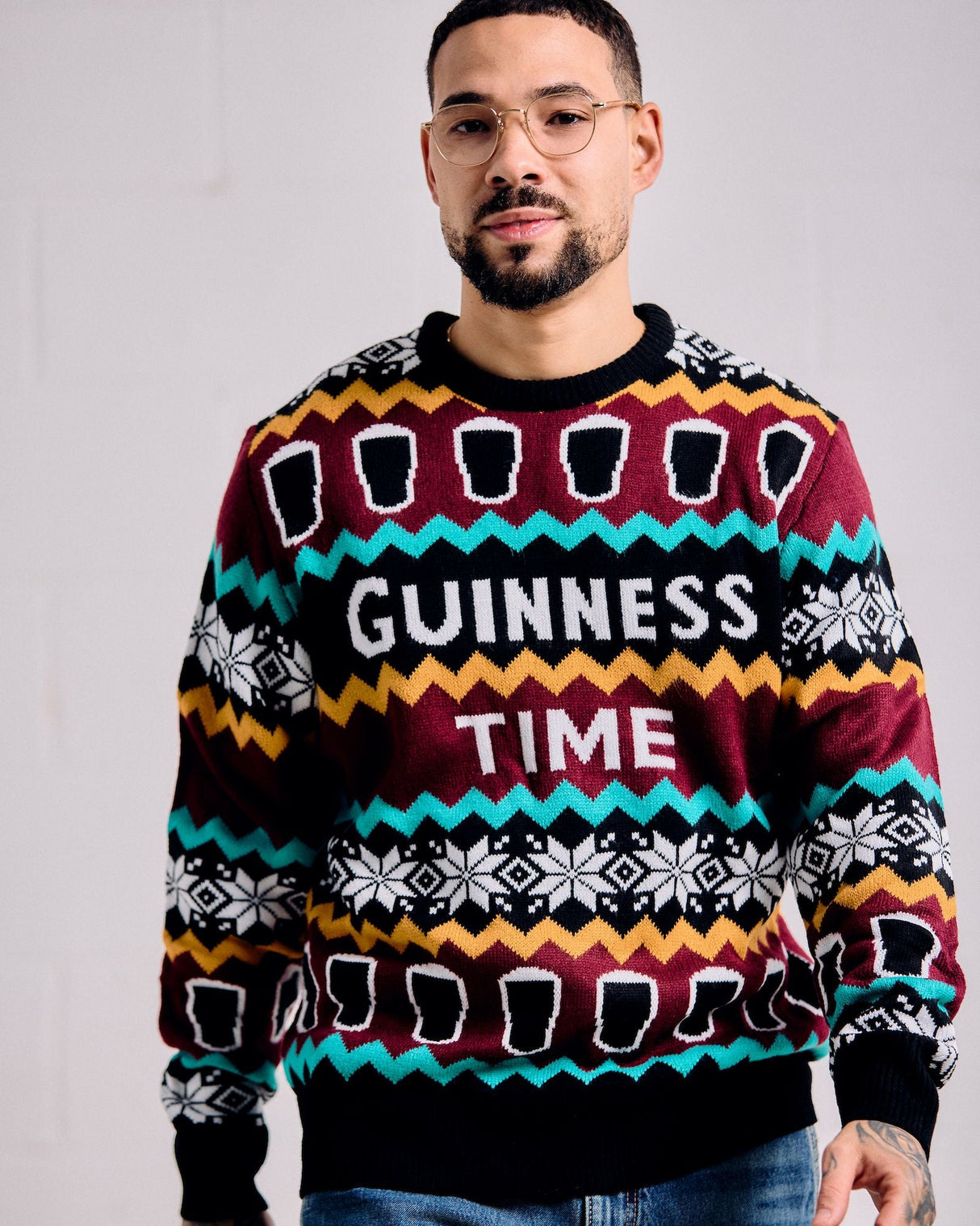 Man wearing a colorful sweater with 'Guinness Time' text against a plain background