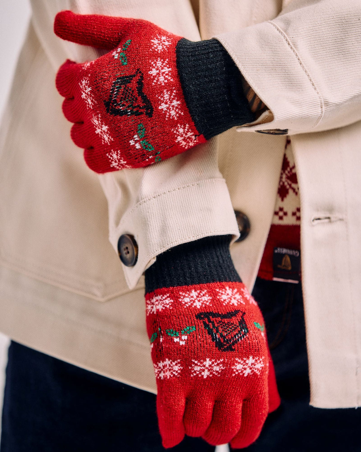 Red gloves with festive design worn by a person in a beige coat.