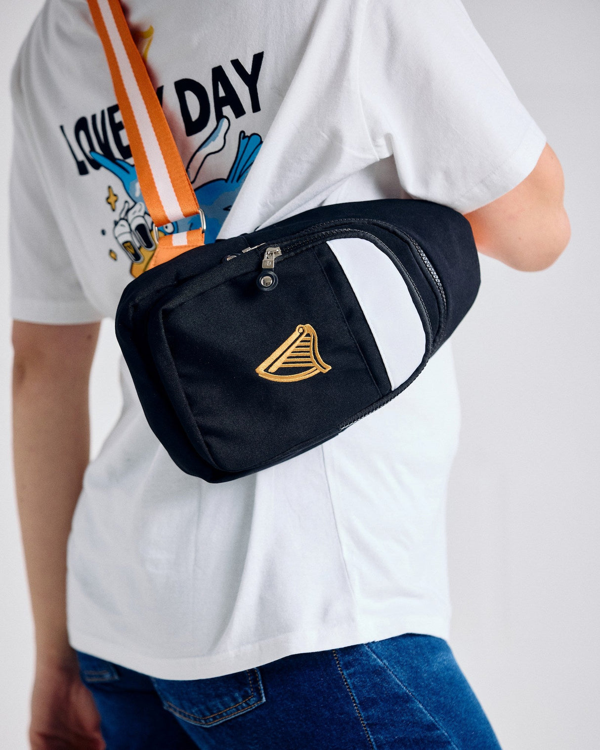 Person wearing a black fanny pack with a gold logo on a plain background