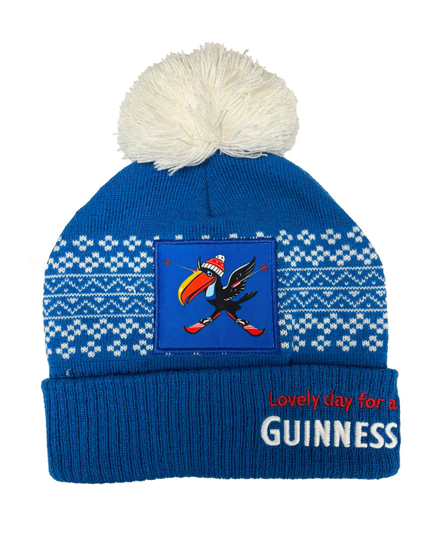 Blue knit beanie with white pom-pom, Guinness logo, and text on a white background