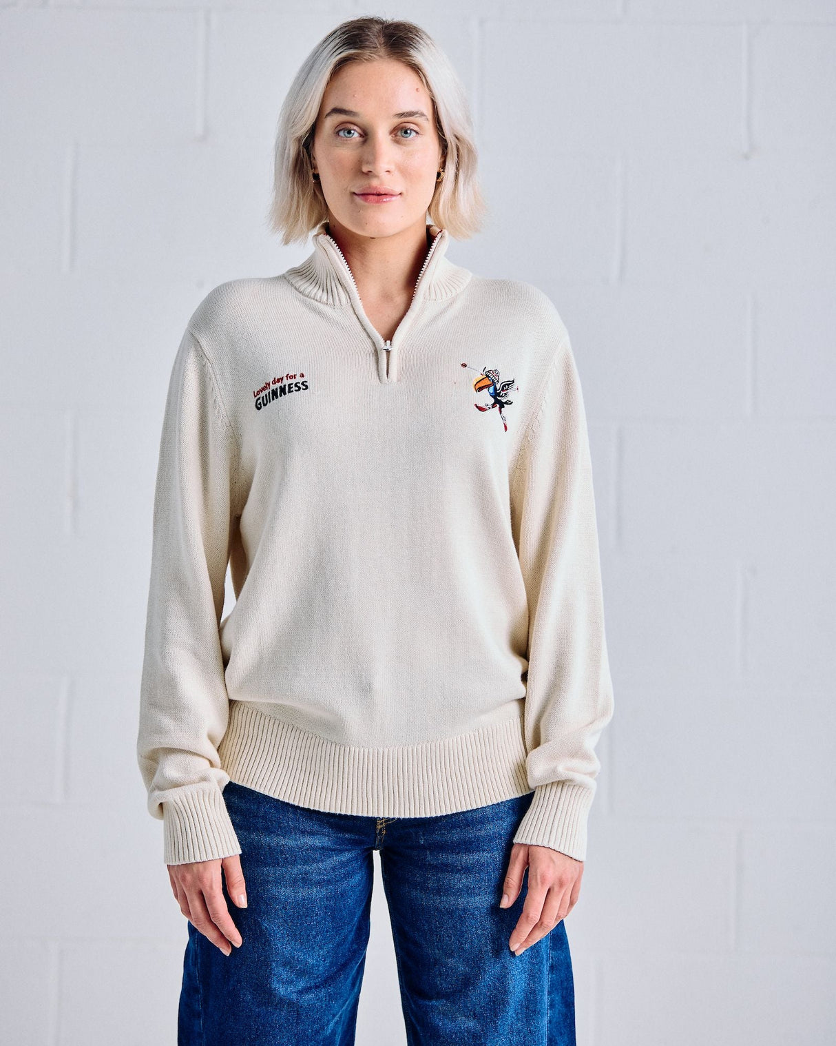 Woman wearing a cream-colored sweater with a logo against a white background