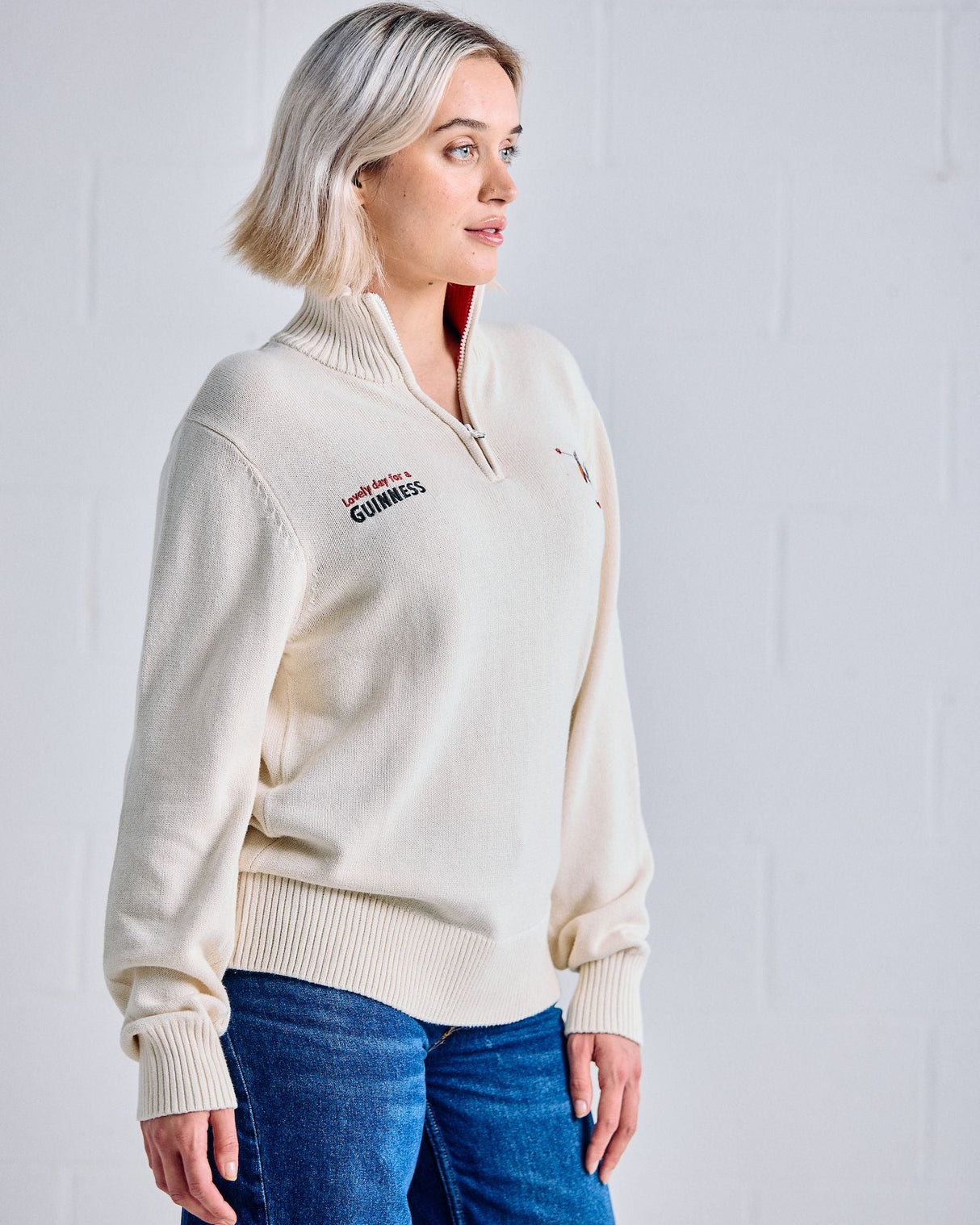 Woman wearing a cream-colored sweater with a brand logo against a light background