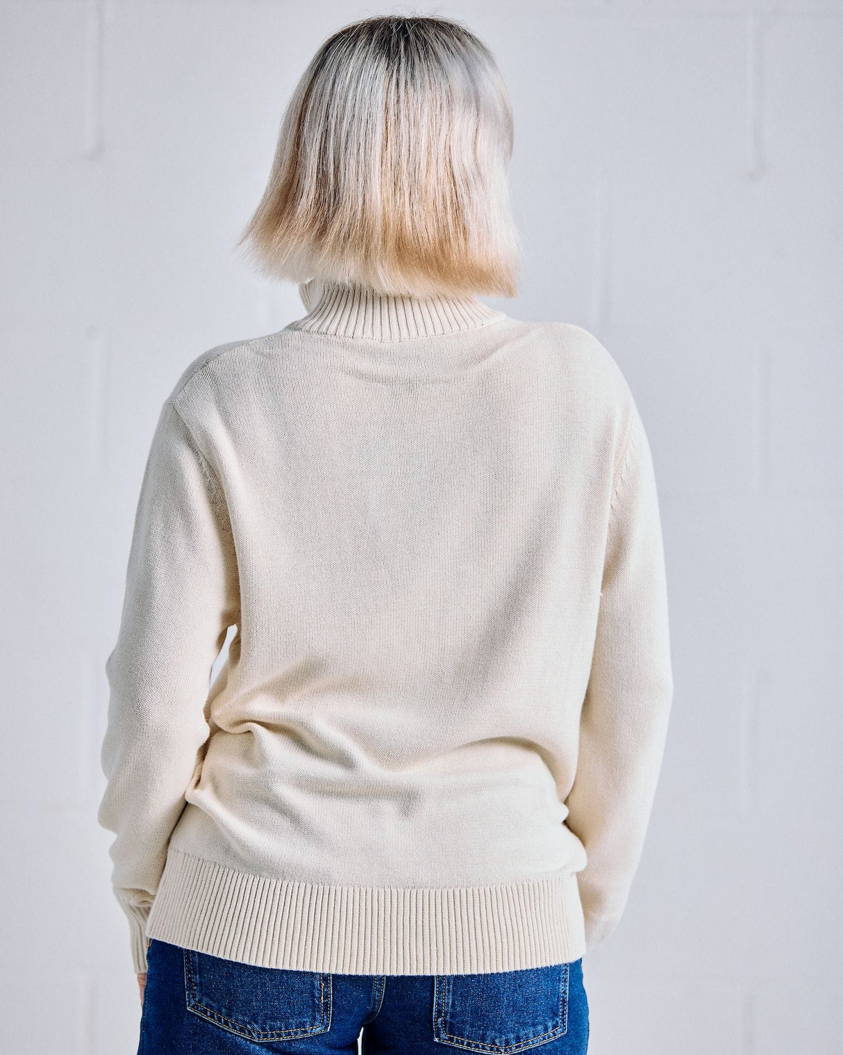 Person wearing a cream sweater and blue jeans against a white background