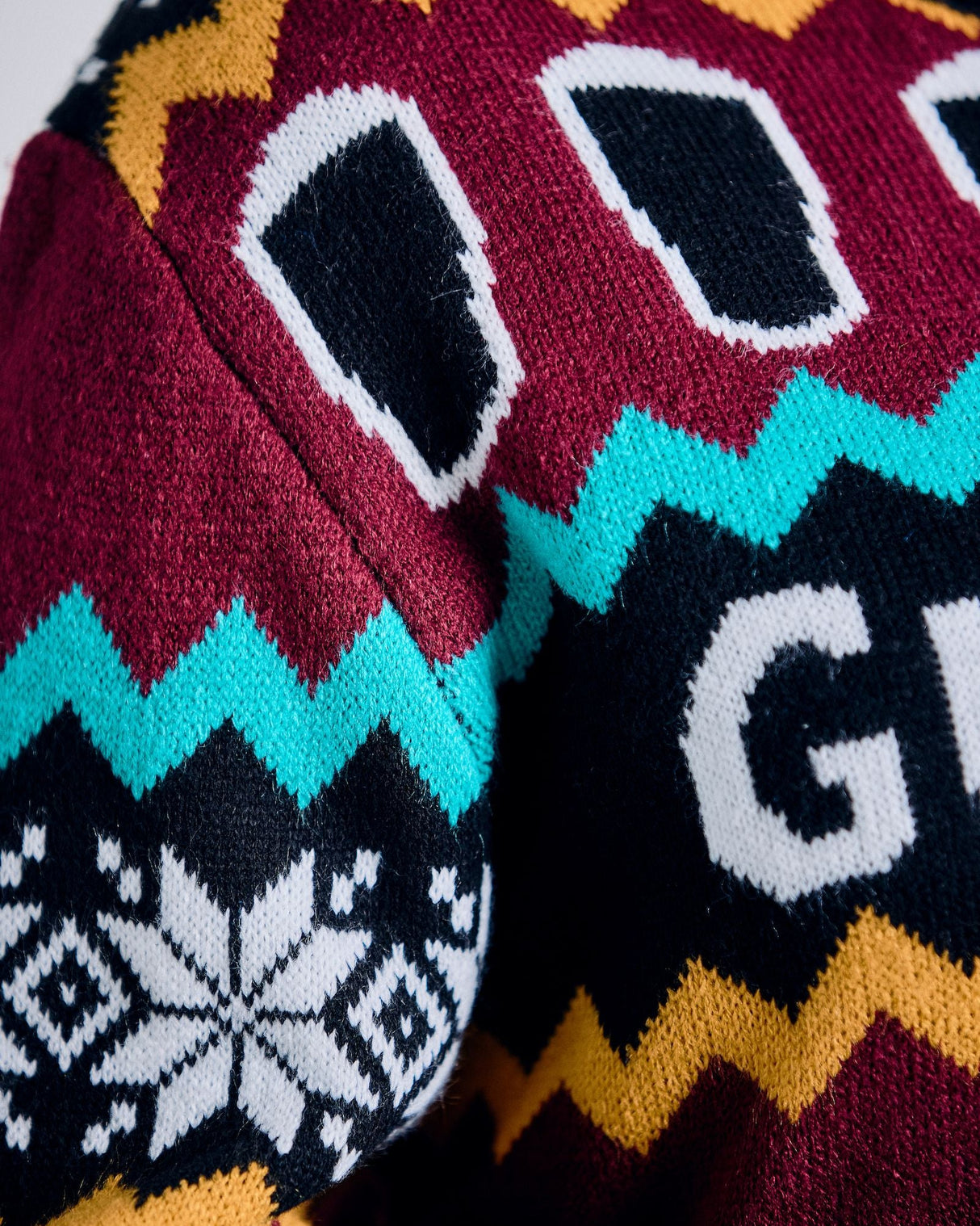 Close-up of a colorful knitted sweater with geometric patterns and text.