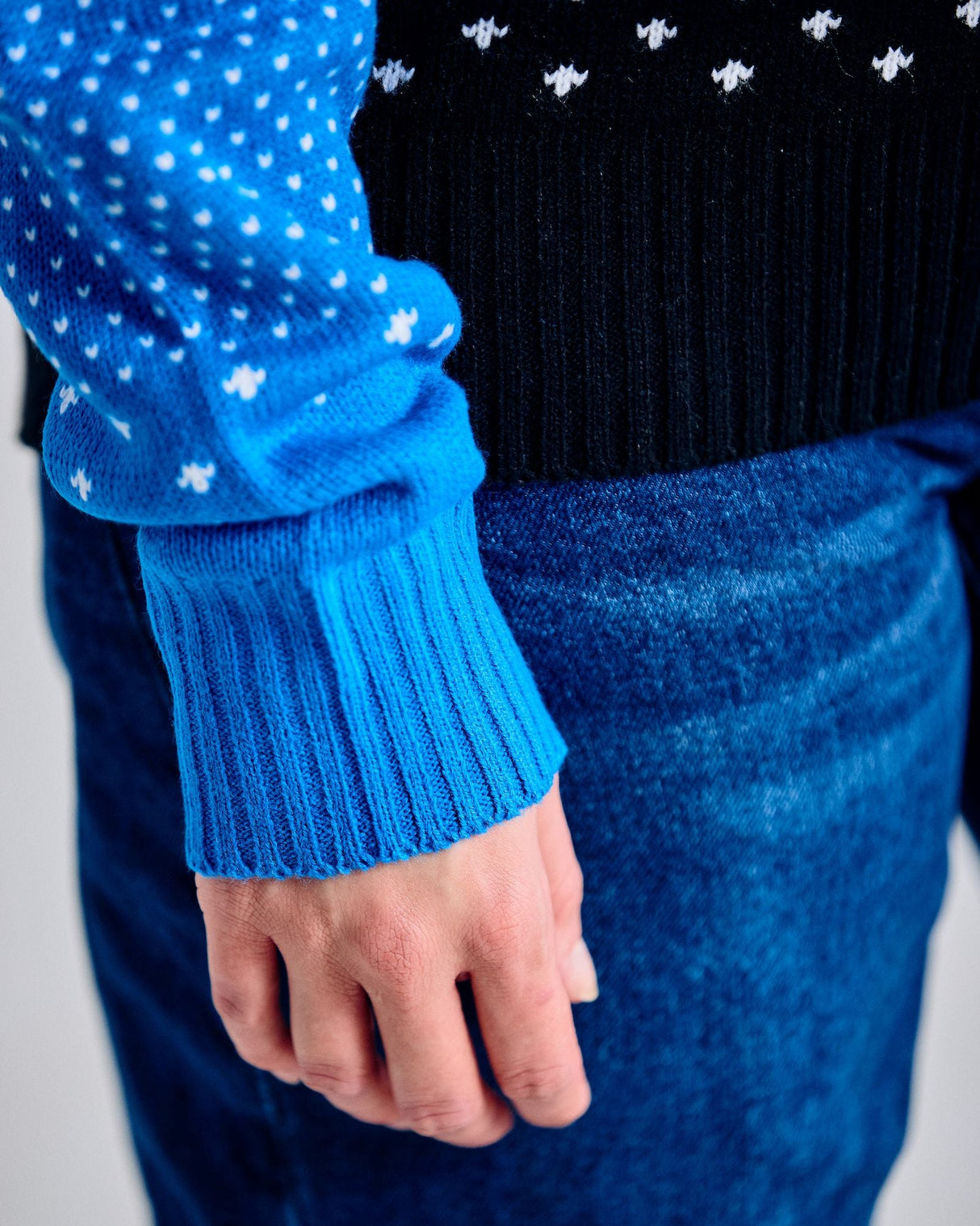 Close-up of blue knitted sleeves with white patterns on a black sweater and blue pants.