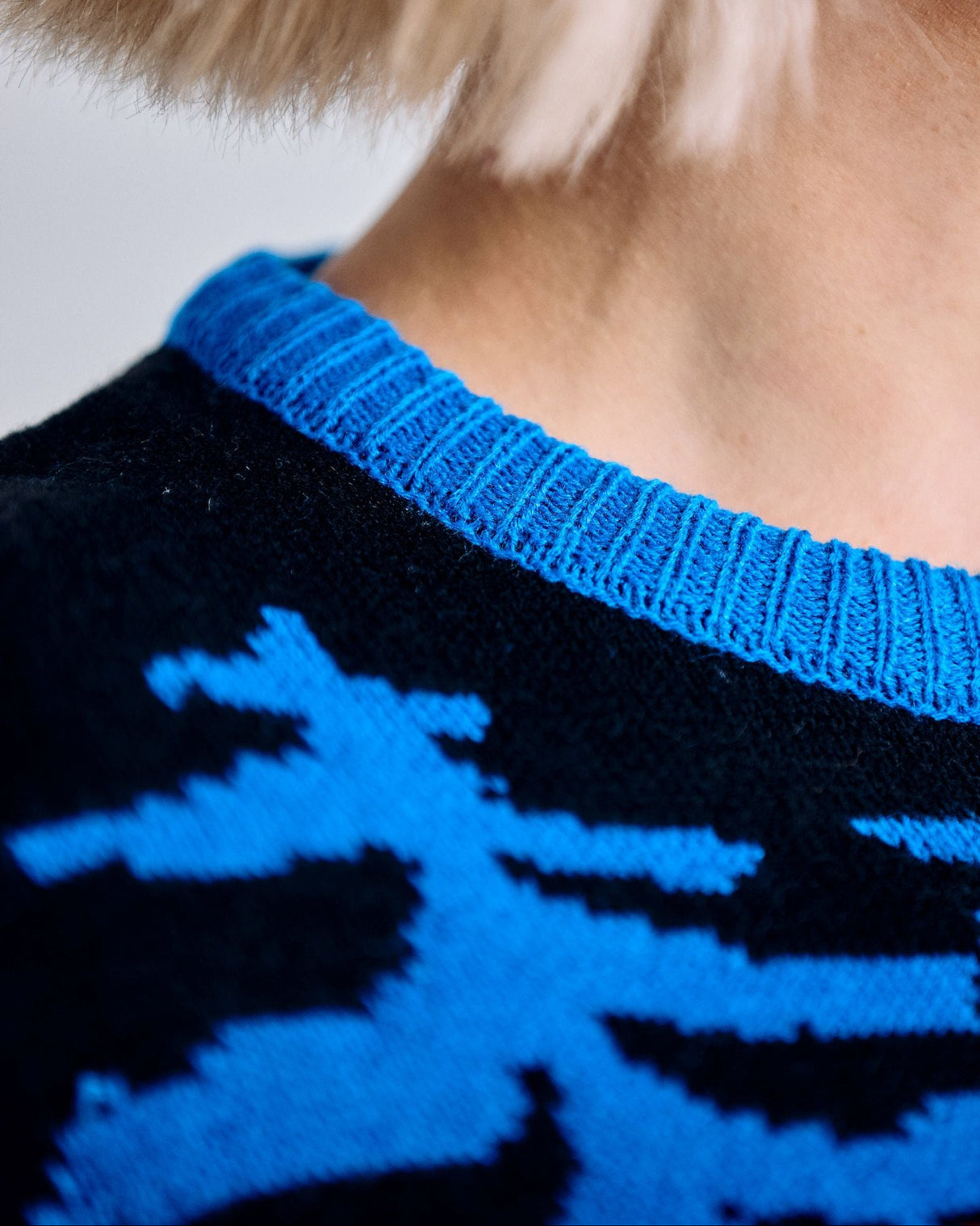 Close-up of a person wearing a black sweater with blue pattern and trim.