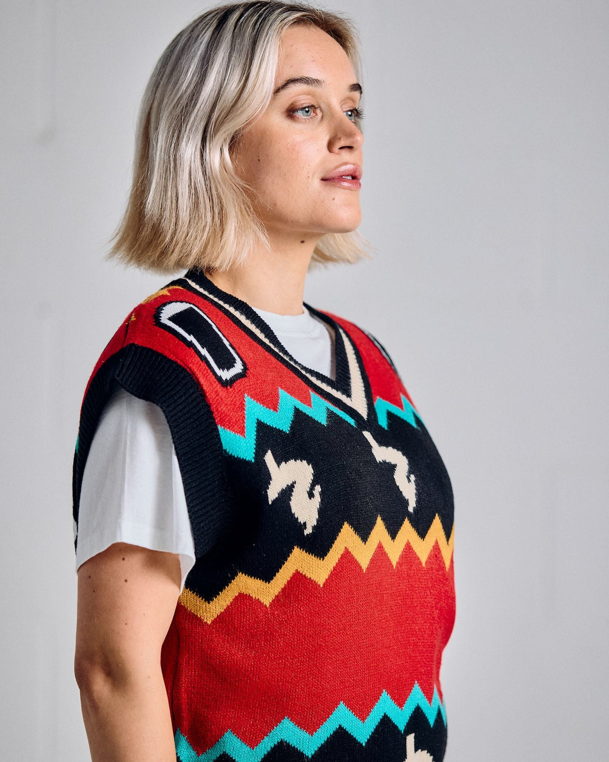 Person wearing a colorful patterned sweater vest against a plain background