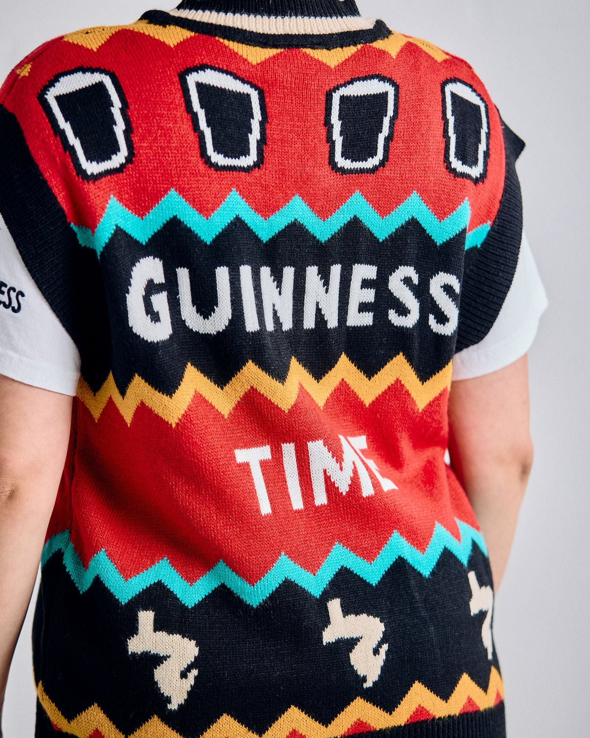 Person wearing a colorful Guinness-themed sweater vest with text on a plain background