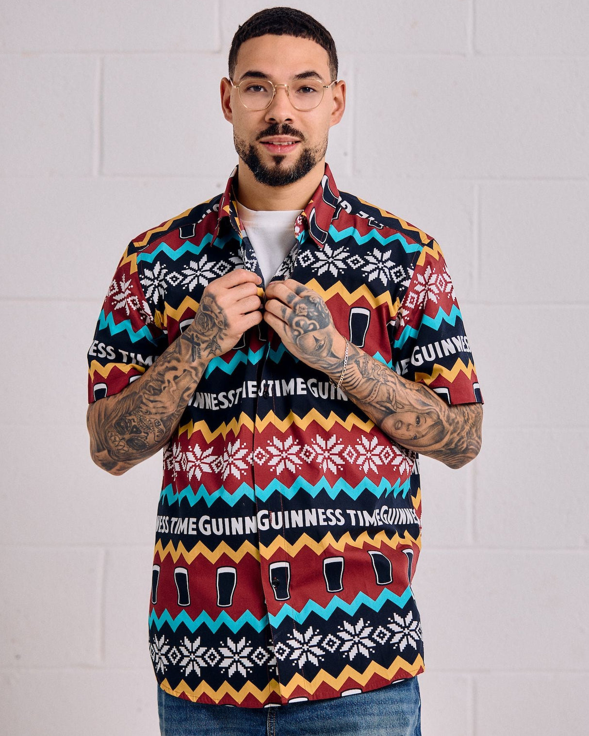 Man wearing a colorful patterned shirt with visible branding against a white brick wall.