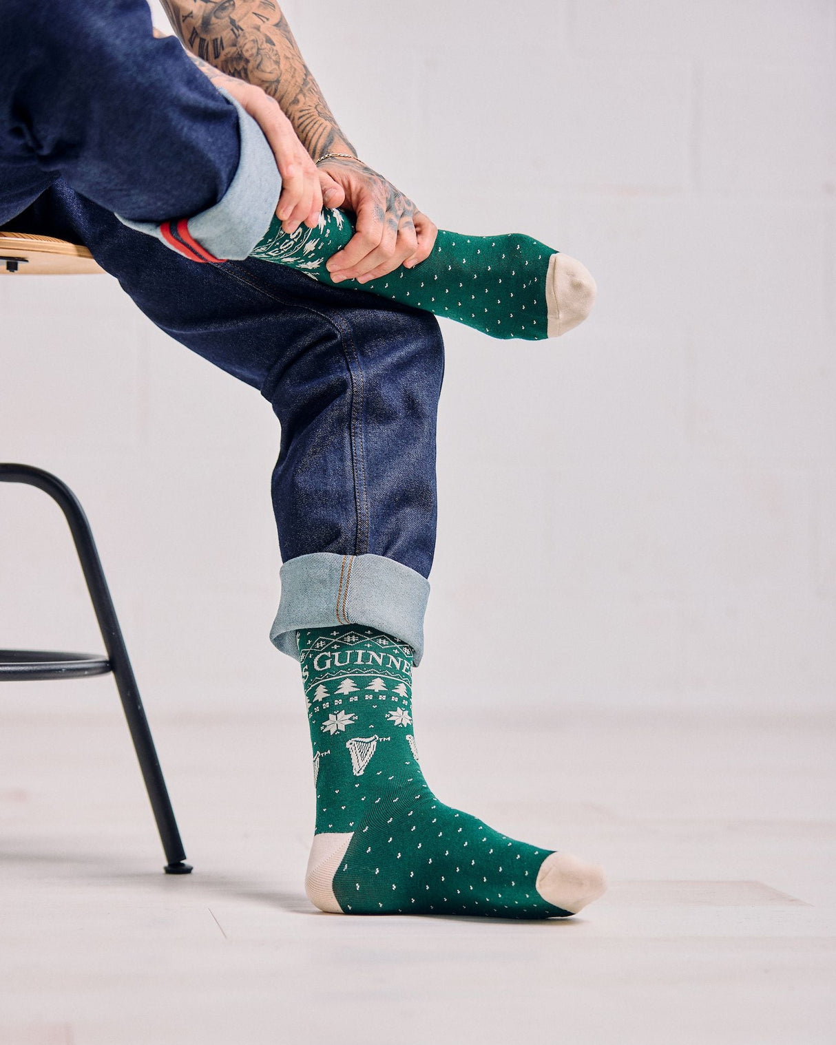 Person wearing green socks with a pattern, sitting on a chair against a plain background
