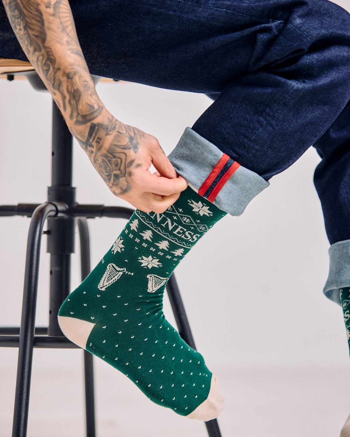 Person wearing a green sock with white patterns, sitting on a stool.