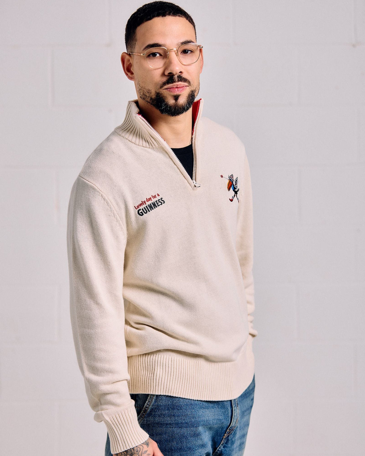 Man wearing a cream-colored sweater with brand logos on a plain background