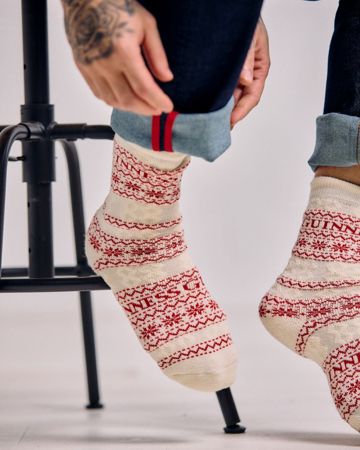 Person wearing patterned socks with a visible brand name, sitting on a stool.