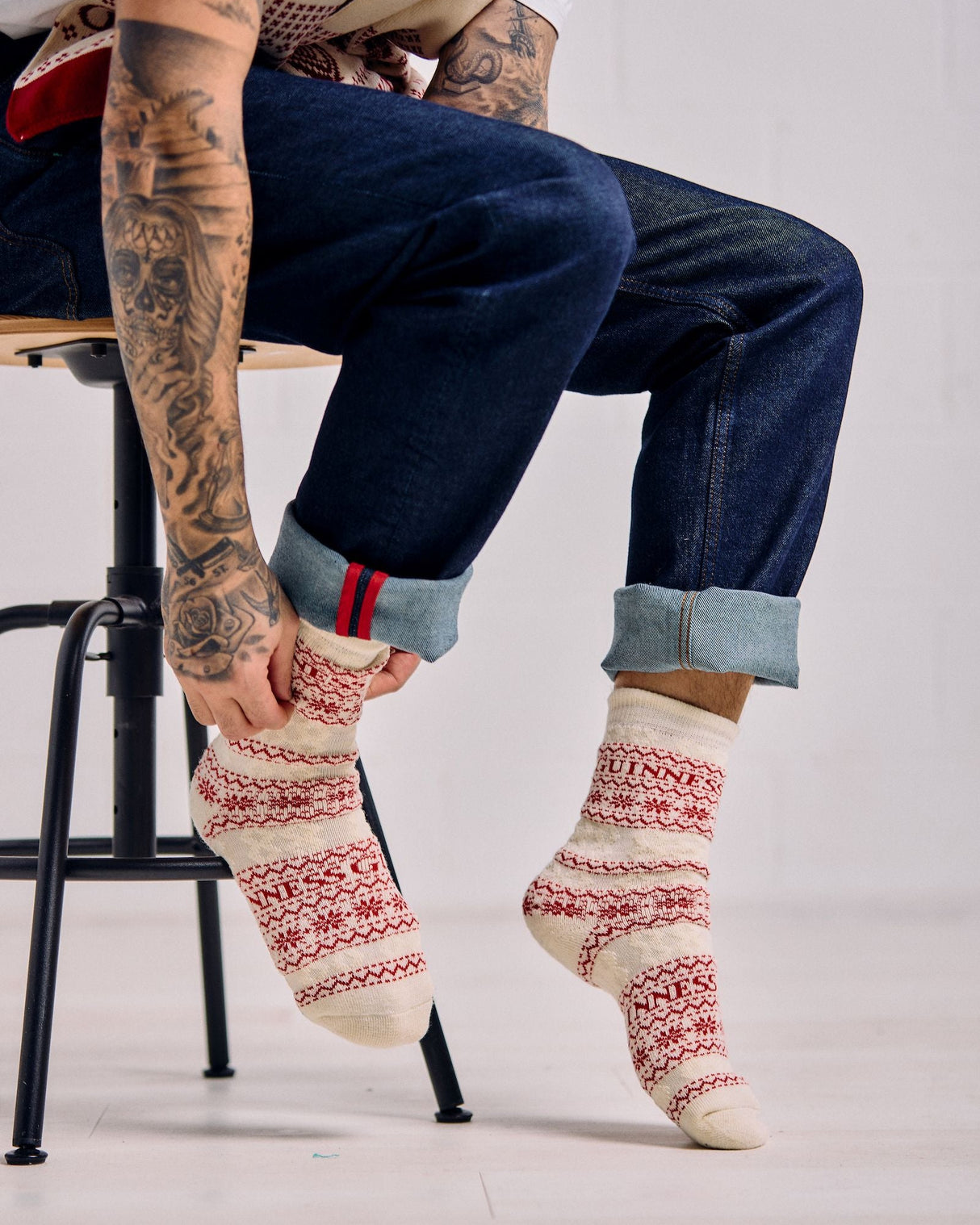 Person wearing patterned socks and blue jeans sitting on a chair.