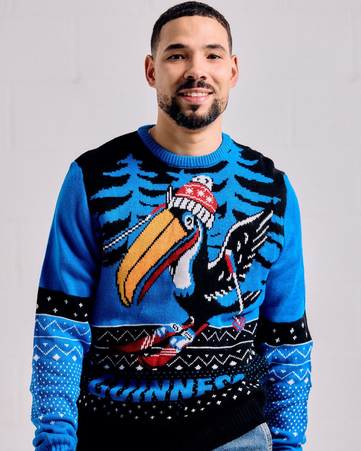 Man wearing a blue sweater with a colorful design of a bird and text, standing against a plain background.