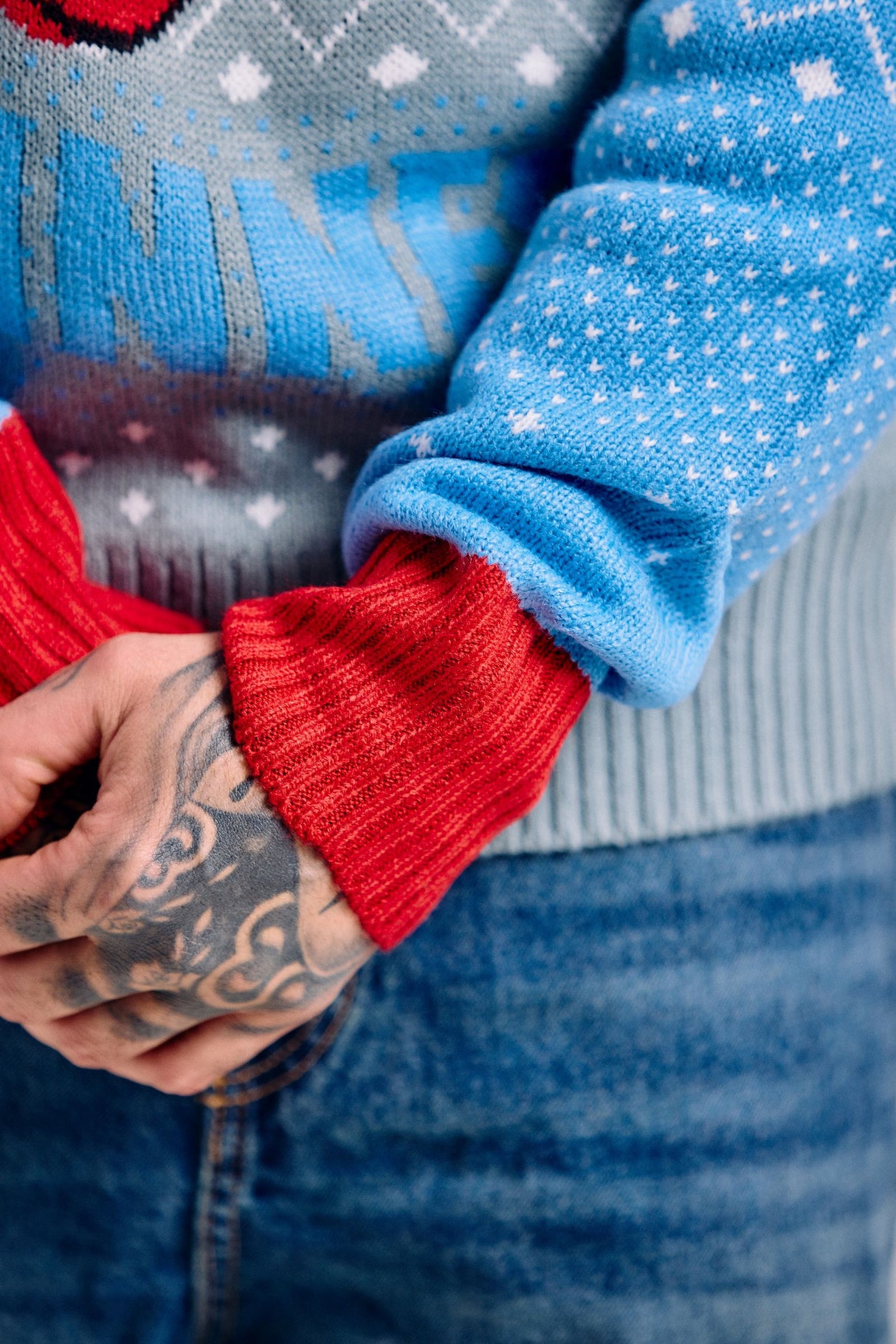 Close-up of two people holding hands, one wearing a red sweater and the other a blue sweater with a pattern.