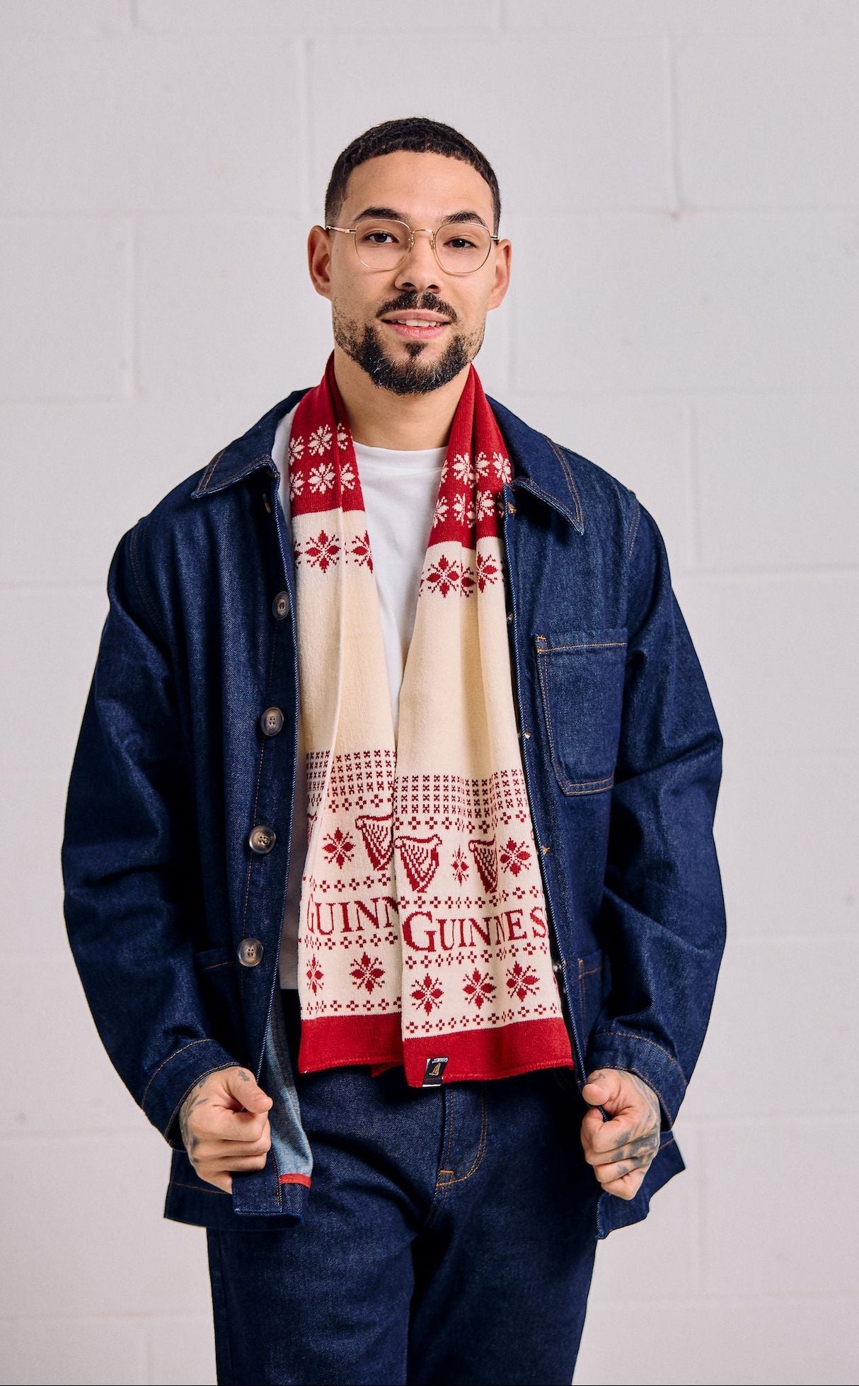 Man wearing a blue denim jacket and a patterned scarf against a white wall