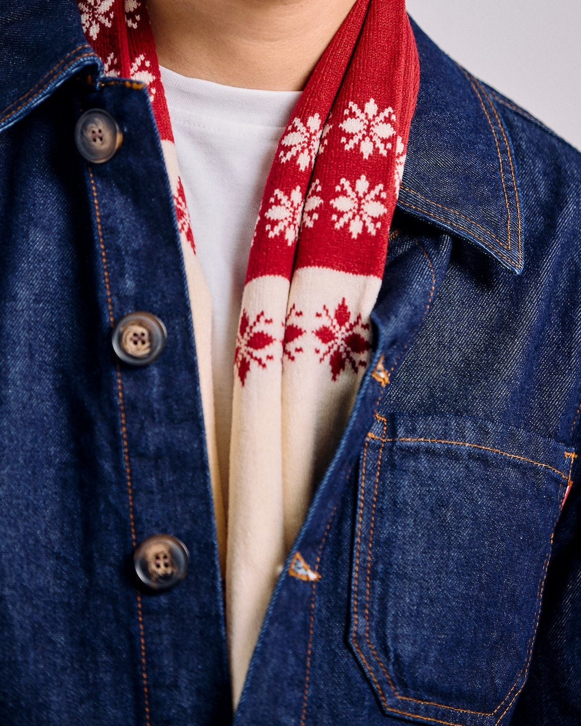 Man wearing a denim jacket, white shirt, and red scarf with white patterns on a plain background
