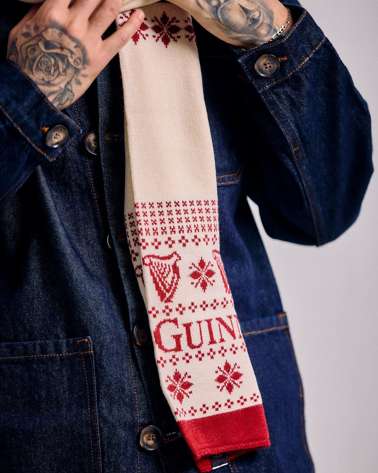 Person wearing a denim jacket with a patterned scarf featuring the Guinness logo.
