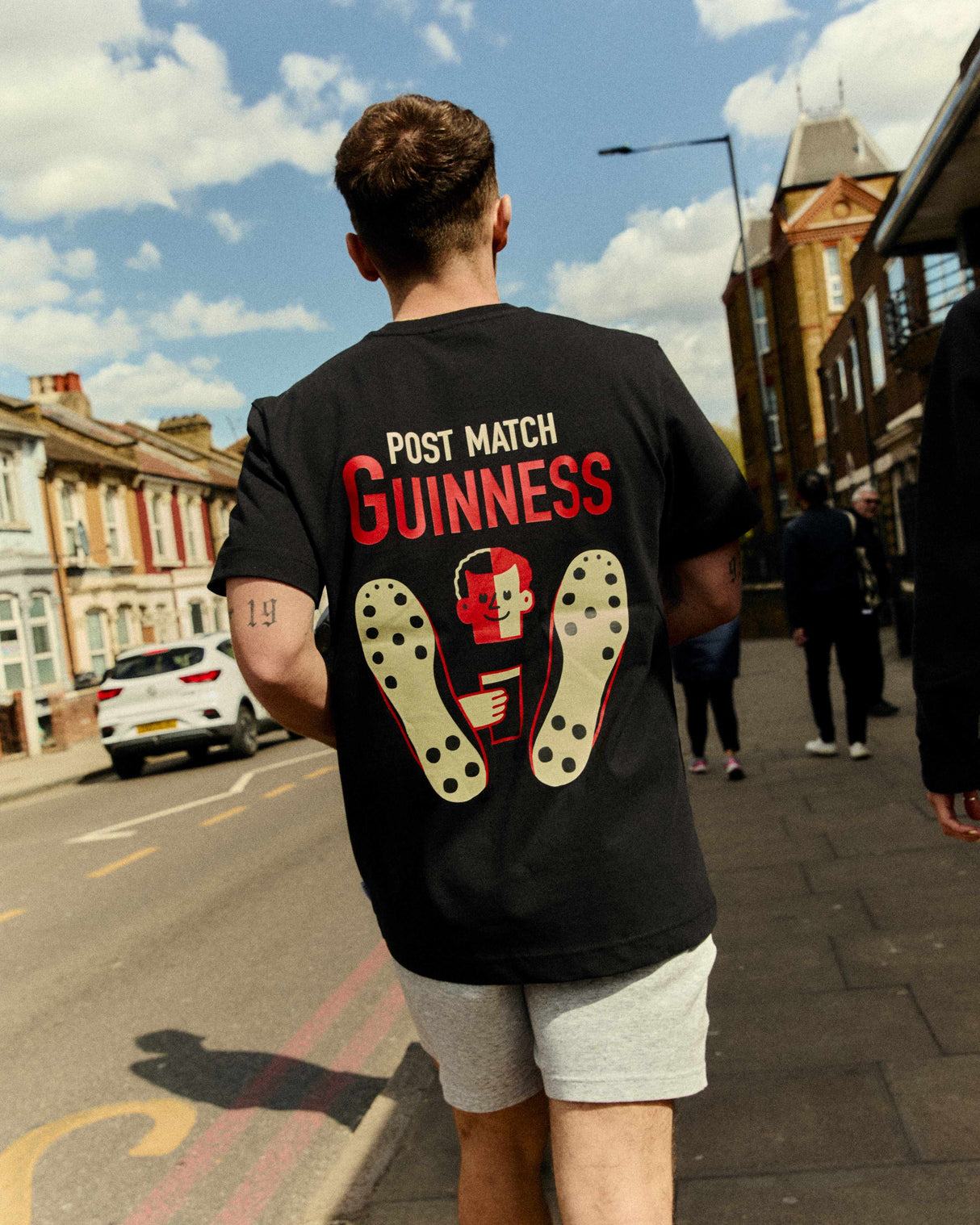 Person wearing a black t-shirt with 'Post Match Guinness' text and graphics on a street.