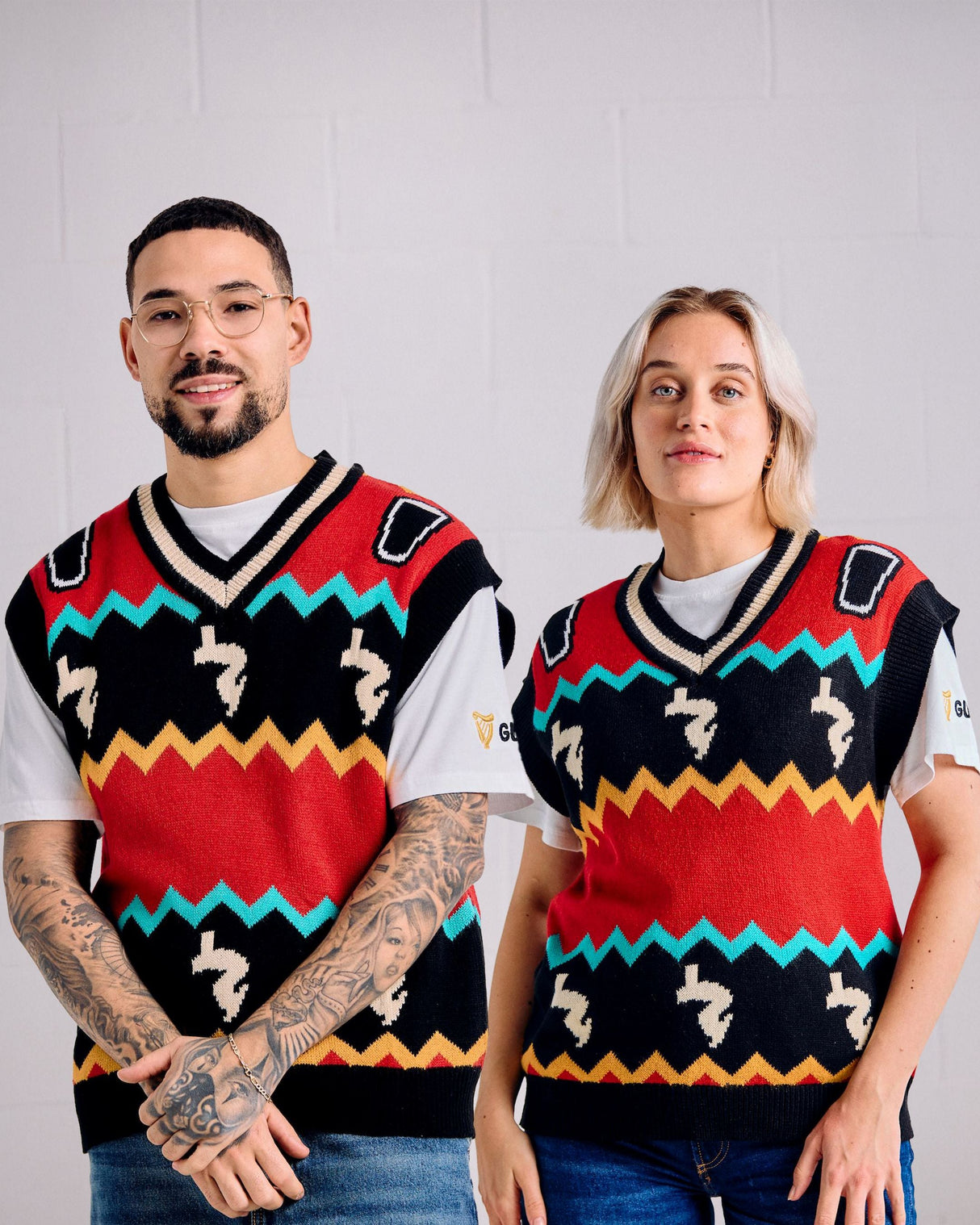 Two people wearing colorful patterned vests against a plain background