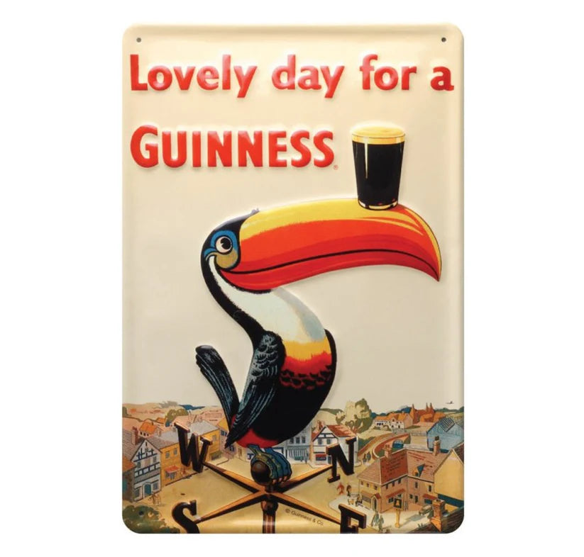 A metal sign featuring an illustration of a toucan with a pint of Guinness, with the text 'Lovely day for a GUINNESS' on a backdrop depicting a cityscape.