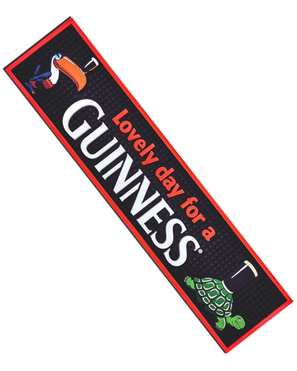 A rectangular Guinness PVC bar mat with red and green trim. It features the iconic Guinness toucan and text 'Lovely day for a GUINNESS' as well as an image of a turtle.